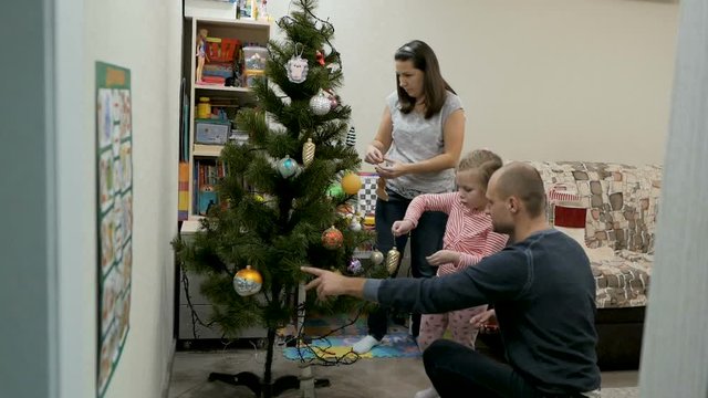 Happy family decorating a Christmas tree with boubles in the living-room