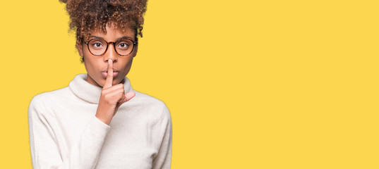 Beautiful young african american woman wearing glasses over isolated background asking to be quiet with finger on lips. Silence and secret concept.