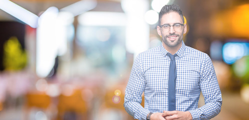 Young business man wearing glasses over isolated background Hands together and fingers crossed smiling relaxed and cheerful. Success and optimistic