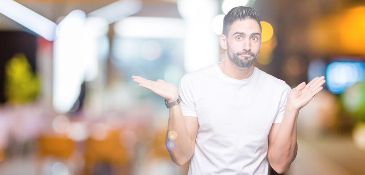 Young man wearing casual white t-shirt over isolated background clueless and confused expression with arms and hands raised. Doubt concept.