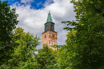 Medieval Turku Cathedral clock tower surrounded by greenery on beautiful summer day in Finland.