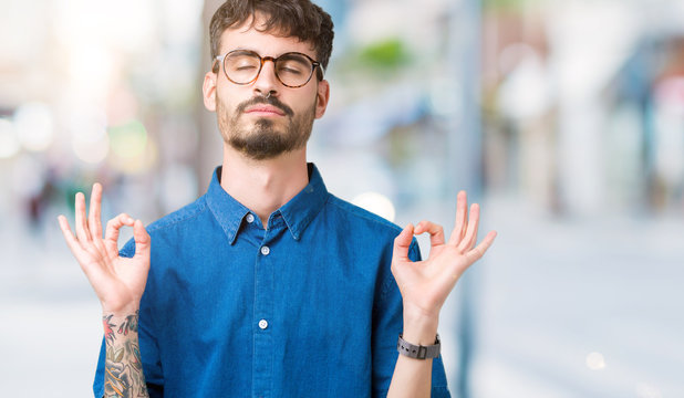 Young handsome man wearing glasses over isolated background relax and smiling with eyes closed doing meditation gesture with fingers. Yoga concept.