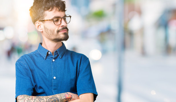 Young handsome man wearing glasses over isolated background smiling looking to the side with arms crossed convinced and confident