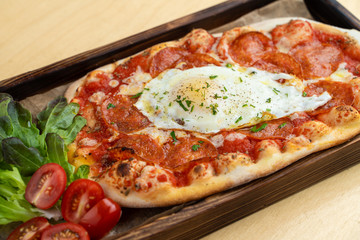 Classic rome pizza with crust, tomato sauce, spicy pepperoni and fried egg in the centre, served on wooden tray