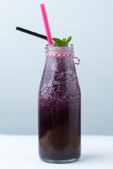 Blueberry smoothie with banana and berry juice in a bottle with straws