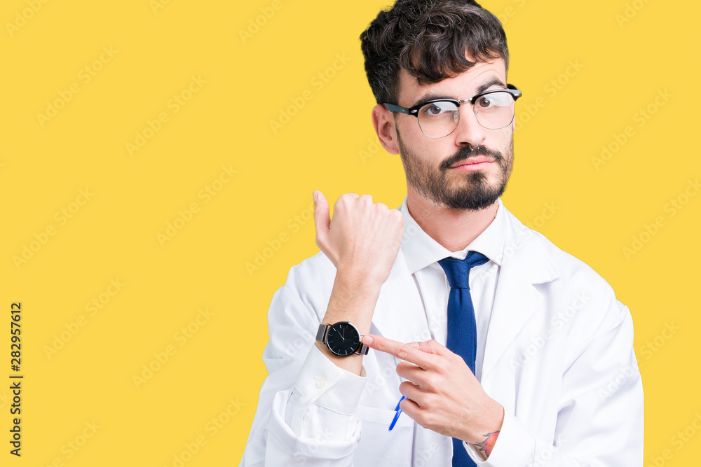 Wall mural young professional scientist man wearing white coat over isolated background in hurry pointing to wa