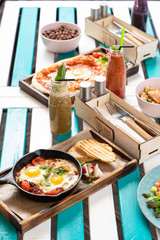 Breakfast outdoors: shakshuka with salami and tomatoes and italian pizza with fried egg and pepperoni, served with seasonal smoothies