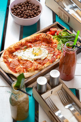 Breakfast on the summer terrace: pizza with tomato sauce, spicy pepperoni and fried egg with seasonal smoothies and chocolate cereal
