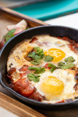 Close up of traditional israeli breakfast: shakshuka with tomatoes, salami, chili pepper and fried eggs, served in hot cast pan with toasts