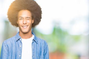 Young african american man with afro hair winking looking at the camera with sexy expression,...