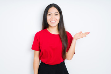 Beautiful brunette woman wearing red t-shirt over isolated background smiling cheerful presenting and pointing with palm of hand looking at the camera.
