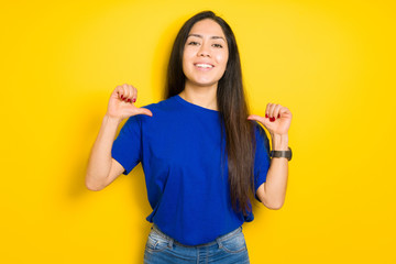 Beautiful brunette woman wearing blue t-shirt over yellow isolated background looking confident with smile on face, pointing oneself with fingers proud and happy.