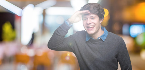 Young handsome elegant man over isolated background very happy and smiling looking far away with hand over head. Searching concept.