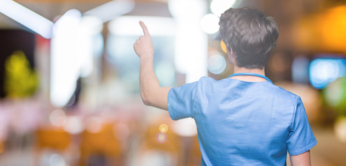 Young doctor wearing medical uniform over isolated background Posing backwards pointing behind with finger hand