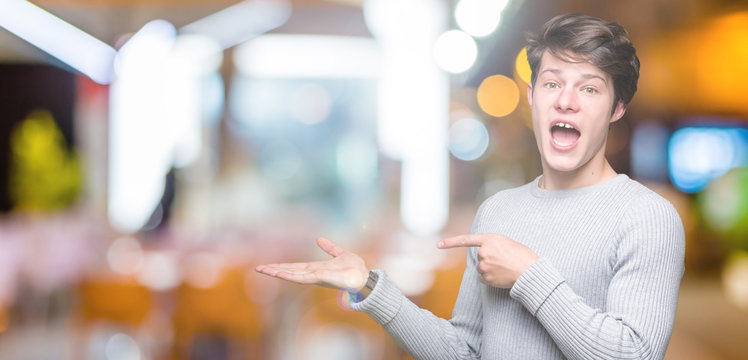 Young handsome man wearing winter sweater over isolated background amazed and smiling to the camera while presenting with hand and pointing with finger.