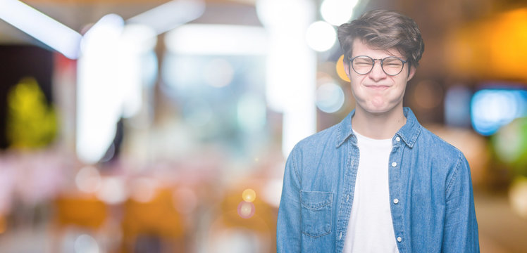 Young handsome man wearing glasses over isolated background puffing cheeks with funny face. Mouth inflated with air, crazy expression.