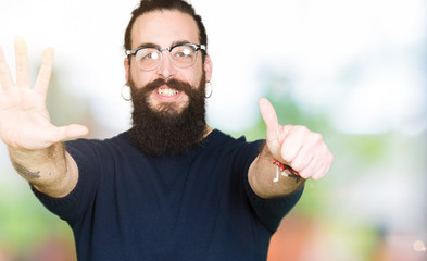 Young hipster man with long hair and beard wearing glasses showing and pointing up with fingers number six while smiling confident and happy.