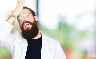 Doctor therapist man with long hair and bear wearing white coat surprised with hand on head for mistake, remember error. Forgot, bad memory concept.