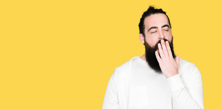 Young man with long hair and beard wearing sporty sweatshirt bored yawning tired covering mouth with hand. Restless and sleepiness.