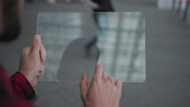 Young man holding futuristic transparent tablet computer in hand holographic screen visual effects outdoors airport in the street modern tech application communication innovation slow motion