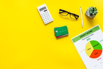 credit score with credit cards and calculator, glasses on banker work place yellow background top view mock up