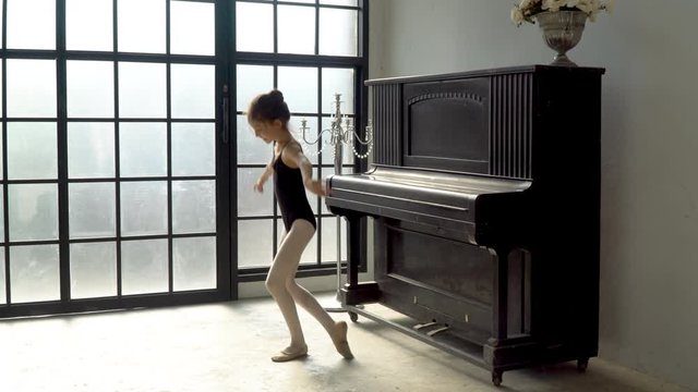 4K Tracking wide shot happy little cute child girl dancer in black leotard and ballet slipper shoes jumping and dancing contemporary ballet dance at vintage studio room