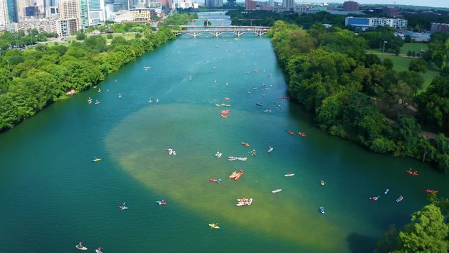 4K Cinematic Aerial Footage of people on Kayaks and Paddleboards on the river River Panning up to Reveal a cityscape with skyscrapers 