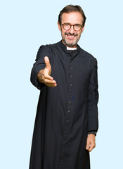 Middle age priest man wearing catholic robe smiling friendly offering handshake as greeting and...