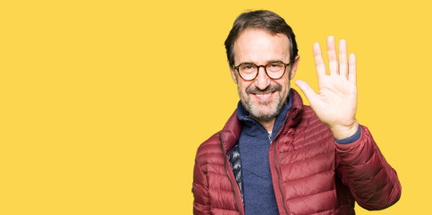 Middle age handsome man wearing glasses and winter coat Waiving saying hello happy and smiling,...