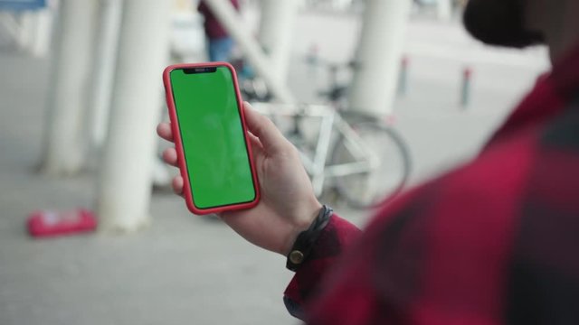 Attractive hands man holding a smartphone touching phone with vertical green screen red case on background walk near airport street message business male device digital equipment internet slow motion