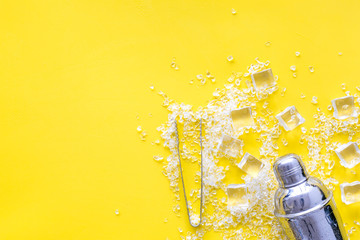 Frozen water in ice cubes and shaker on yellow bar table top view mockup