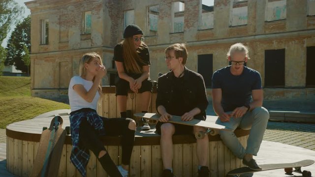 Stylish Cool Teenagers Chilling on the Benches in the Park. Two Girls and Two Boys Resting with Their Skateboards, Talking and Having Fun. Stylish Post Industrial Park In Gentrified Part of City
