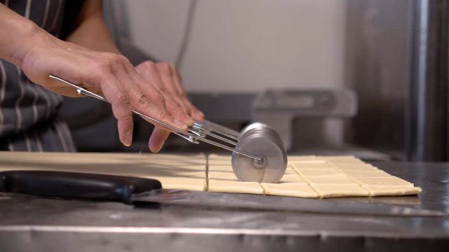 Pastry chef cutting croissant dough with kitchen utensil on stainless steel bench in patisserie bakery