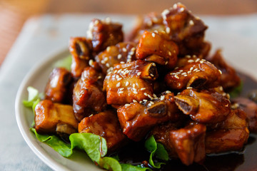 Close up of a plate of sweet and sour pork ribs with white sesame seeds
