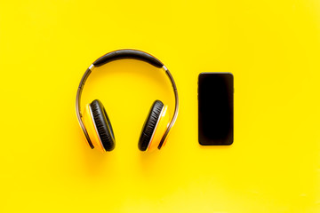 Wireless headphones and mobile phone as music gadgets on yellow background top view