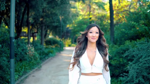 Beautiful Asian girl walking and smiling in the park. She is wearing white dress. Happy video