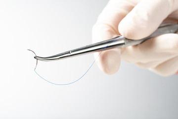Doctor holding needle holder on white background. Suture thread. Nylon surgical thread. - obrazy, fototapety, plakaty