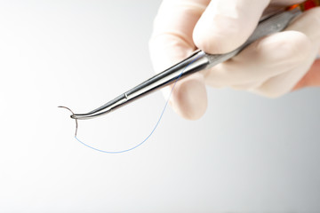 Doctor holding needle holder on white background. Suture thread. Nylon surgical thread.