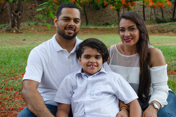 couple of Latin American men and women, with boy suffers autism, happy in a portrait family outdoors together in a park, the three laughing hugging