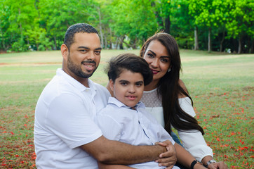 couple of Latin American men and women, with boy suffers autism, happy in a portrait family outdoors together in a park, the three laughing hugging