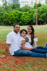 couple of Latin American men and women, with boy suffers autism, happy in a portrait family outdoors together in a park, the three laughing hugging