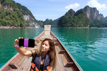 Fototapeta na wymiar Asian woman taking selfie on wooden boat with mountains background