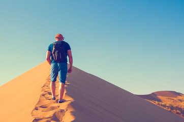 A man with backpack  goes up on sand dune. Desert landscape