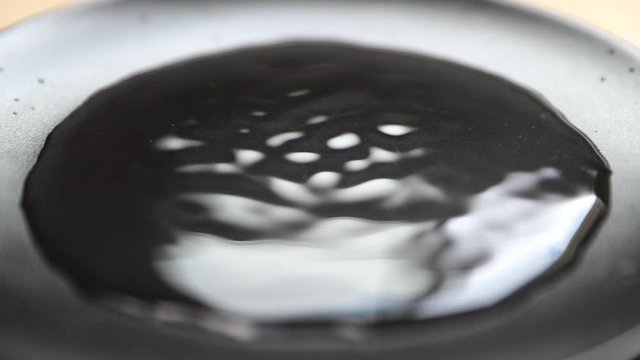 Water drop capture in slow motion on close up macro camera when it hit vodn&iacute; hladinu a pomalu se rozpust&iacute; do stran on dark backgound plate with light reflection.