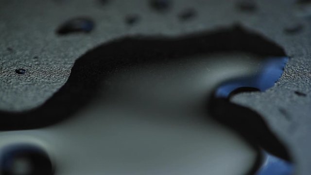 Water drop capture in slow motion on close up macro camera when it hit vodn&iacute; hladinu a pomalu se rozpust&iacute; do stran on dark backgound plate with light reflection.