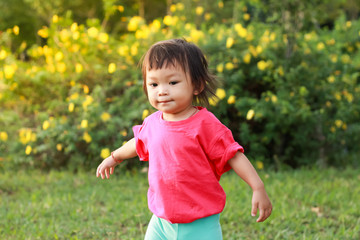 Portrait image of happy Asian baby girl aged of 1 year and 5 months old. She walking in the flowers garden backyard. Summer season with sunlight and kid. Sweet smiling. Development of child concept.