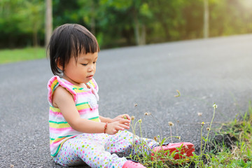 Soft focus, Portrait image of 1 year and 5 months baby. In the summer season happy Asian child girl relaxing and sitting on flowers grass floor in the garden resort. Kids and travel concept.