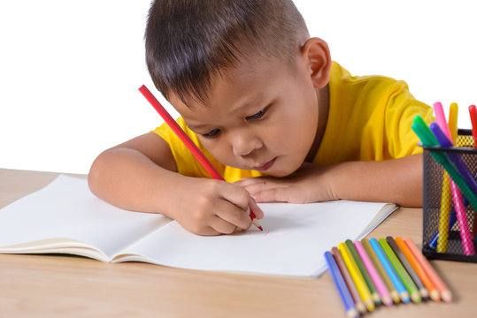 Cute cheerful child drawing using color pencil while sitting at table isolated on white background