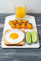 fried egg on toast with cucumbers, cherry tomatoes and orange juice. Light healthy breakfast