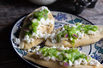 Mexican tlacoyos with green sauce on wooden background